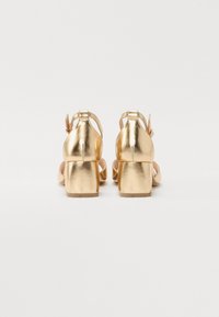 Gouden metallic high heels met enkelbandjes en blokhakken, met een gladde textuur en een minimalistisch design.