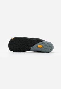 Semelle de chaussure noire et grise avec un motif de grip texturé. Présente un logo de marque jaune proéminent et une forme unique pour une meilleure adhérence.