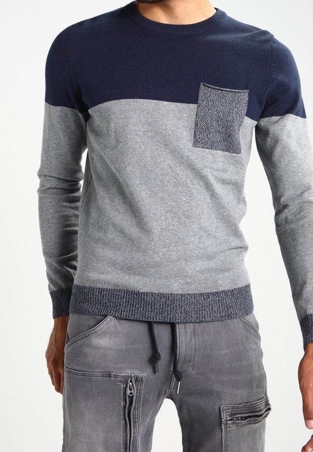 Pull en tricot bleu marine et gris avec un design à fente horizontale, poche poitrine texturée et poignets et ourlet côtelés. Associé à un pantalon cargo gris.
