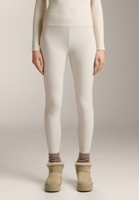 Witte leggings met een hoge tailleband, gemaakt van gladde stof, gecombineerd met tan laarzen met een voering van bont en geribde wol sokken.