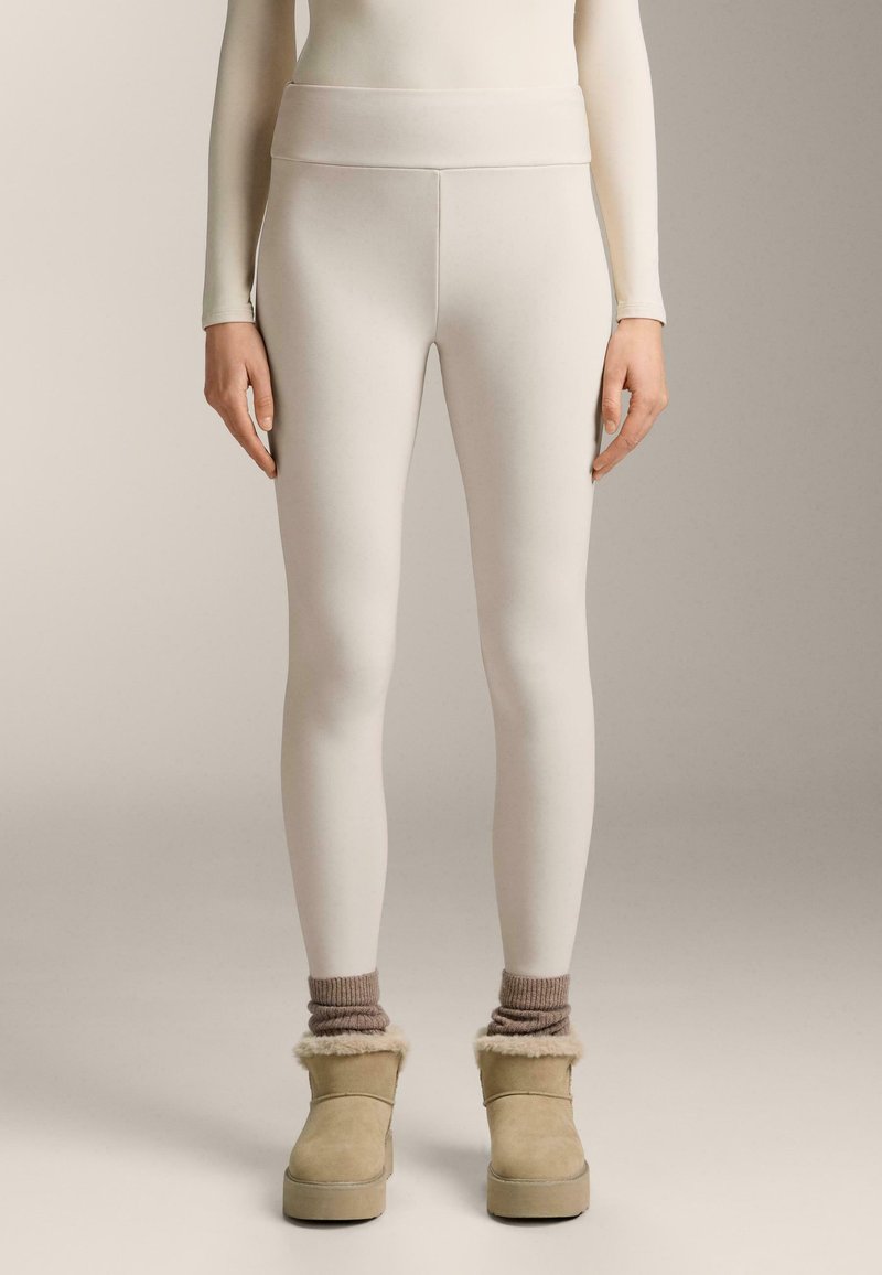 Witte leggings met een hoge tailleband, gemaakt van gladde stof, gecombineerd met tan laarzen met een voering van bont en geribde wol sokken.