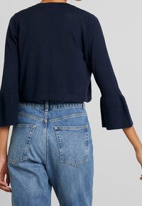 Pull cropped marine avec des manches évasées, texture en tricot et encolure ronde, associé à un jean en denim bleu clair taille haute avec poches arrière.