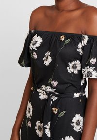 Černé šaty bez ramínek s bílým a růžovým květinovým vzorem, s elastickým výstřihem a vázáním v pase pro přiléhavý siluetu.