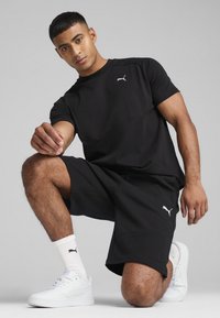 Svart atletisk T-shirt och shorts med en elegant design och Puma-logotyp. Matchade med vita skor och strumpor som framhäver rena linjer.
