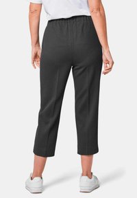 Zwarte, cropped broeken van een textuurstof, met een elastische tailleband en zijslits, gecombineerd met witte sportschoenen.