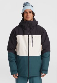 Skijack met een zwarte capuchon en bovenstuk, crème middenstuk en teal onderstuk. Zacht materiaal met ritsafsluiting en verstelbare manchetten.