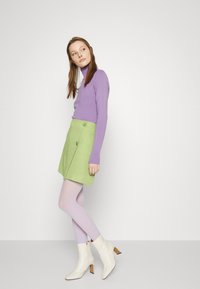Suéter longo roxo, saia verde em linha A com detalhes de botão, collants lilás claros e botas brancas até o tornozelo com salto quadrado.