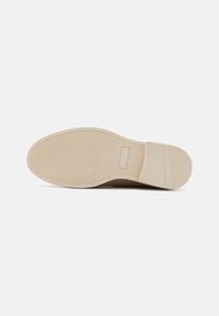 Suela de zapato de goma beige con patrón texturizado y bordes suaves. Presenta una forma plana y estrías verticales para mayor adherencia.