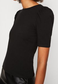 Černý top s krátkým rukávem, kulatým výstřihem a nabíranými balónovými rukávy; vyrobený z hladkého, pružného materiálu.