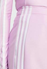 Tejido atlético de color rosa claro con tres rayas blancas verticales a lo largo del costado, textura suave, diseño ajustado y un ajuste ceñido en la cintura.