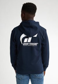 Felpa navy con tasca a marsupio, caratterizzata da un ampio logo bianco Gran Turismo e testo sul retro; tessuto morbido e polsini a costine.