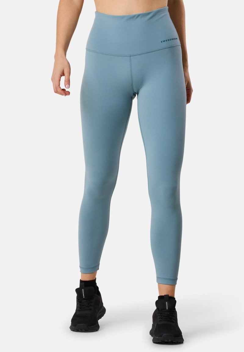 Leggings taille haute bleu clair fabriqués en matériau extensible, avec une texture lisse et une subtilité de marque sur la ceinture.