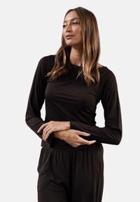 Czarny longsleeve z gładkiego materiału, z prostym okrągłym dekoltem i luźnym krojem. Modelka pozująca z rękami skrzyżowanymi.