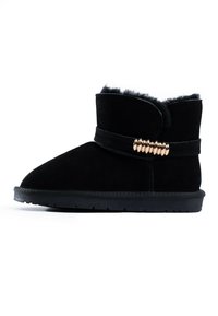 Botín negro de ante con forro de piel sintética, diseño de slip-on y un acento decorativo de hardware dorado alrededor del tobillo. Suela de goma plana.
