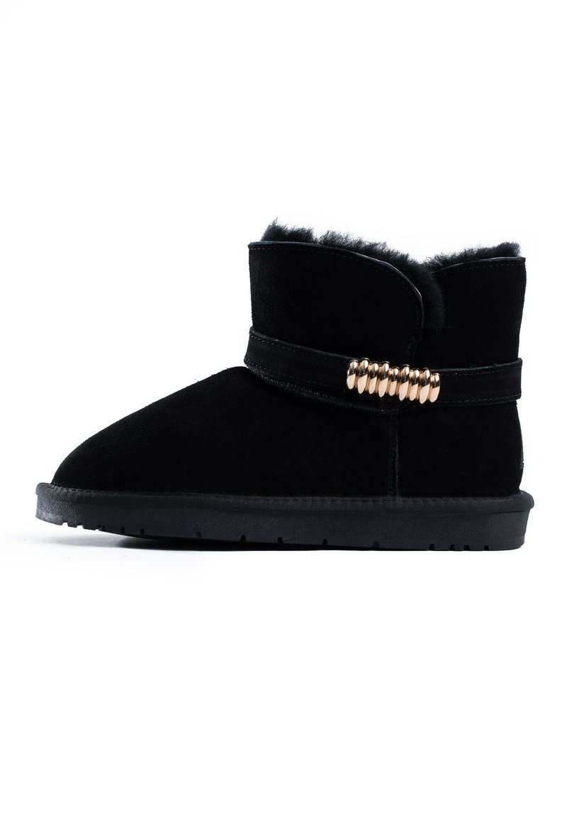 Botín negro de ante con forro de piel sintética, diseño de slip-on y un acento decorativo de hardware dorado alrededor del tobillo. Suela de goma plana.