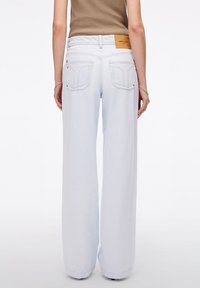 Jeans de pernera ancha en azul claro, hechos de denim, con bolsillos traseros, una tela texturizada y un parche de logo marrón en la cinturilla.