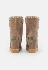 Botas de tobillo de ante marrón con un acabado texturizado, que presentan un borde trenzado, acentos de logotipo metálico y una suela de goma.