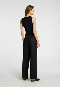 Black sleeveless top with a fitted design paired with high-waisted, loose black trousers and flat black slip-on shoes. Simple, smooth texture.