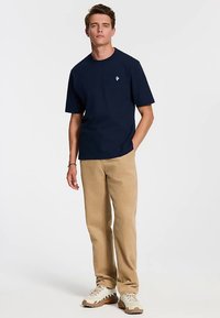 Tumesinise puuvillane T-särk ümarate kaeluste ja lühikeste varrukatega, mis on kombineeritud beežide kõrvetatud pükstega ja kreemjate tossudega. Lihtne disain koos logoga.