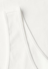Débardeur blanc avec une texture côtelée, des bretelles larges et des coutures contrastantes le long des bords. Matériau en coton doux.