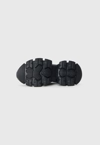Svart fotturse sko såle med dype dekk for grep, med en strukturert design og gummimateriale. Merkbare riller for feste.