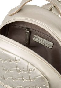 Hellbeige Rucksack mit geprägt Logo, glatter Textur, mit Reißverschluss-Fach und einem dunkelbraunen Innenfutter. Mit einem metallischen Reißverschlusszug.