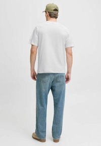 Weißes T-Shirt mit kurzen Ärmeln, kombiniert mit hellblauen Jeans. Das Shirt ist schlicht, und die Jeans haben Gesäßtaschen und einen lockeren Schnitt.
