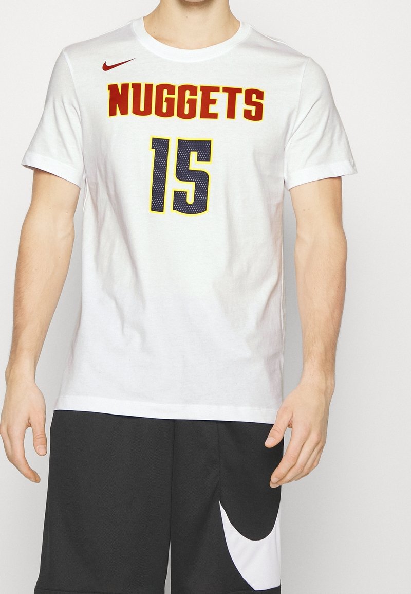 Homme portant un t-shirt blanc des Denver Nuggets avec le numéro 15, et un short de basketball multicolore (rouge, jaune, bleu et noir) avec le logo Nike blanc.