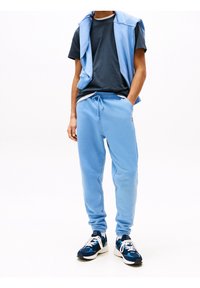 Světle modré joggingové kalhoty s elastickým pasem, doplněné námořnickou tričkem a světle modrou bezrukávovou bundou; černé a modré tenisky.