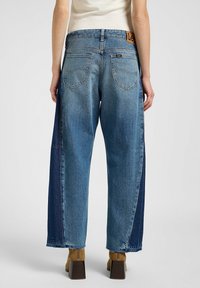 Jeans à jambe large en denim bleu clair avec un panneau contrastant plus foncé, comprenant deux poches arrière et une étiquette de ceinture de marque.