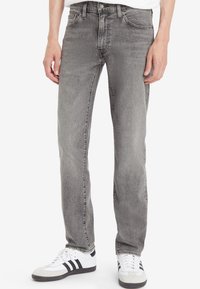 Grå denimjeans med rette ben, fem lommer og subtile slitasjemerker; kombinert med hvite sneakers med svarte striper.