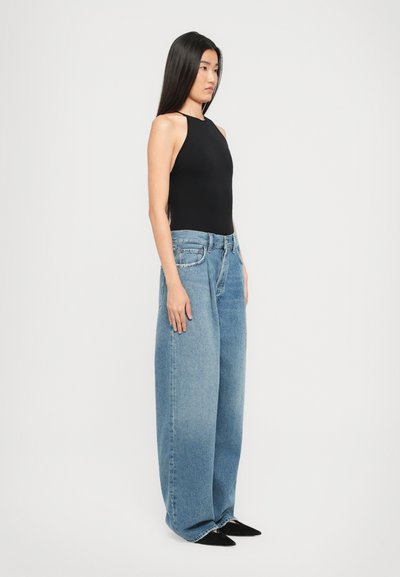 Musthave mustata ja ülikerge helblue kõrge vöökohaga laiad teksad, millel on ees tasku ja kerge pleekimine. Mustad terava ninaöpikud.