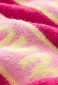 Tissu tricoté en rose vif et jaune, avec une texture douce et moelleuse et des motifs en zigzag. Vue en gros plan montrant le détail du tissage.