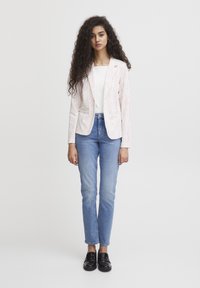Gestreepte blazer in wit en rood, met een enkelvoudige knoopsluiting en twee zakken. Gecombineerd met lichtblauwe jeans en zwarte instappers.