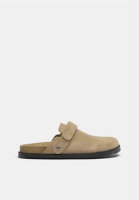 Krémszínű velúr slip-on klumpa kerek orral, patentezáras pánttal és texturált fekete gumitalppal.
