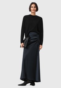 Svart strikket langt skjorte med asymmetrisk design, paret med en mørk sateng maxiskjørt med side ruching og snorjustering.