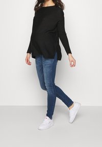 Svart långärmad topp med sidofickor, kombinerad med blå smala jeansa och vita sneakers, med en lös passform för komfort.