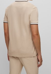 Polo beige à manches courtes, en tissu texturé, avec un bord noir et blanc aux poignets et un détail d'étiquette au dos.