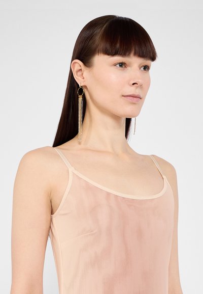 Haut sans manches couleur chair en tissu lisse et semi-transparent ; avec des fines bretelles et une texture dégradée subtile. Longs boucles d'oreilles pendantes avec des chaînes.