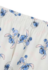 Pantalones cortos blancos con un estampado integral de un personaje alienígena azul con orejas grandes, que sostiene varios objetos, con una suave banda elástica en la cintura.