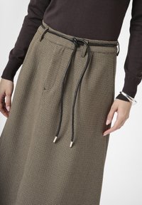 Houndstooth-kuosisella, polven pituista hametta beige- ja ruskeasävyissä, jossa on musta nyöri metallitipoilla ja sivutaskut.