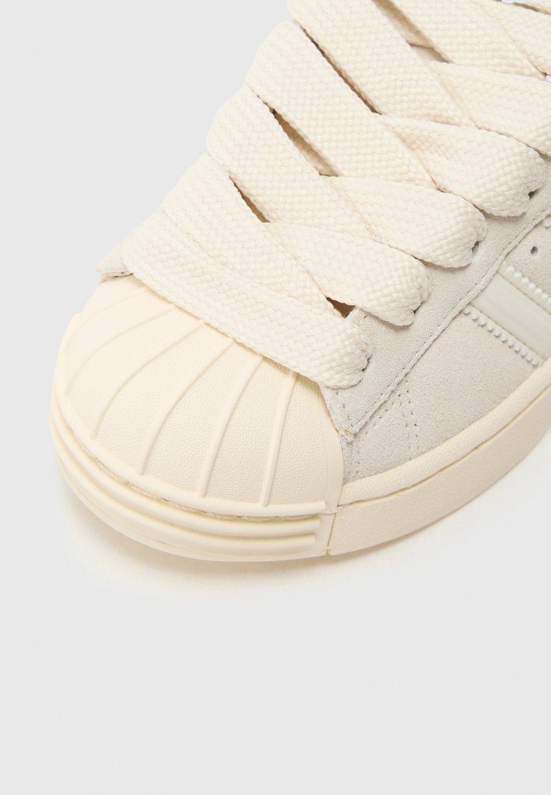 Sneaker color crema con punta in gomma strutturata, lacci intrecciati e tomaia in morbido suede. Presenta cuciture di accento sottili sul lato.