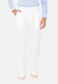 Pantaloni bianchi realizzati in tessuto leggero, con una vestibilità su misura, due tasche laterali e una texture liscia. Abbinati a sneaker bianche e beige.