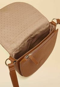 Sac bandoulière en cuir marron avec un extérieur texturé, une poche zippée et une doublure beige clair à pois.
