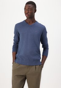 Navy V-Ausschnitt Pullover aus weichem Strickstoff, mit langen Ärmeln und geripptem Saum. Kleines Logo-Detail auf der Brust.