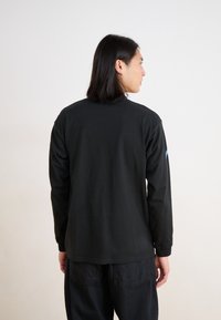 Black long-sleeve shirt in soft fabric with a straight cut. Features minimal design with a colored accent on the sleeve.