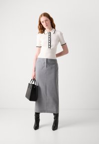 Witte geribbelde polo met zwarte accenten en knopen, gecombineerd met een grijze kokerrok. Zwarte handtas en zwarte laarzen tot de knie.