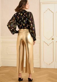 Must mustriga blouse mitmevärviliste täppidega, kombineeritud läikivate kuldsete laia jala pükstega. Mudel kannab musti kontsakingi.