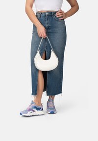 Gonna di jeans con orlo sfrangiato, borsa a forma di mezzaluna bianca e sneakers multicolori con accenti blu, viola e rosa.