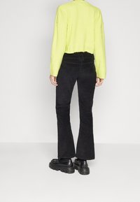 Un pulls cropped côtelé jaune néon associé à un pantalon en velours côtelé noir évasé et des bottes plateformes noires épaisses. Texture lisse dans l'ensemble.